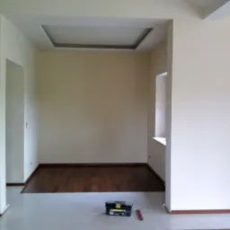 Pomalowane na kremowo wnętrze z drewnianą podłogą, widoczne narzędzia w skrzynce i poziomica, sufit z dekoracyjnym wgłębieniem.